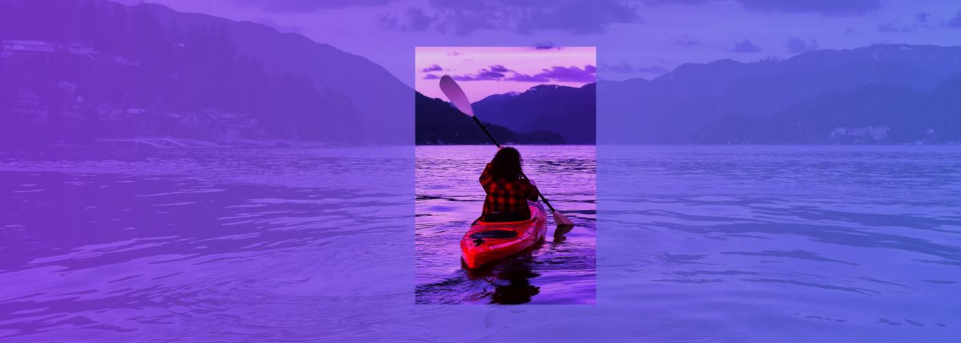 person in canoe in middle of lake with landscape