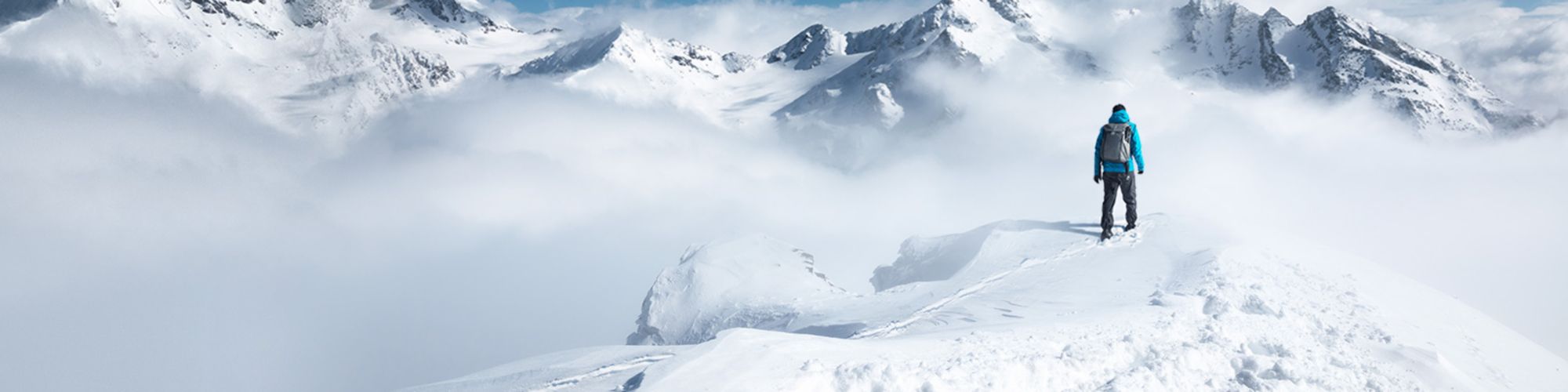 Person steht auf Berg mit Schnee umgeben von Wolken