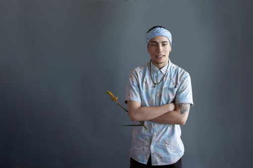 A young male student holding a flower on a grey background