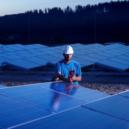 Worker with measuring device checking solar plant in the evening