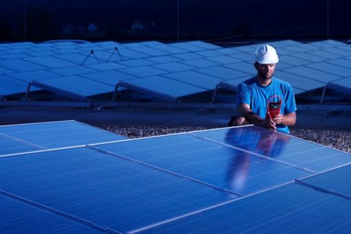 Worker with measuring device checking solar plant in the evening