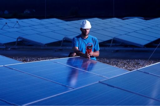 Worker with measuring device checking solar plant in the evening