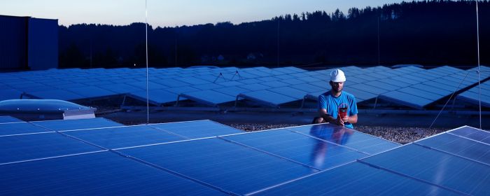 Worker with measuring device checking solar plant in the evening