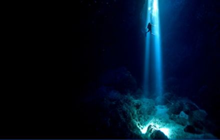 Scuba diver inside cenote swimming up to surface