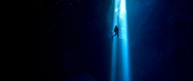 Scuba diver inside cenote swimming up to surface