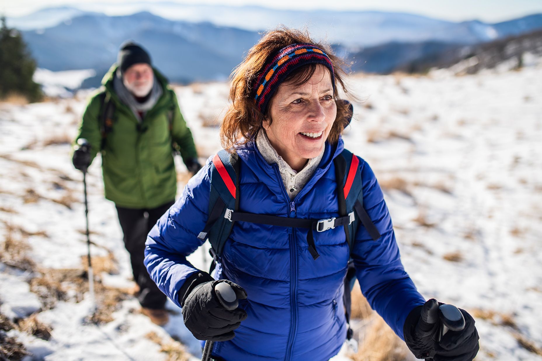 Senior couple with nordic walking poles hiking in snow-covered winter nature.