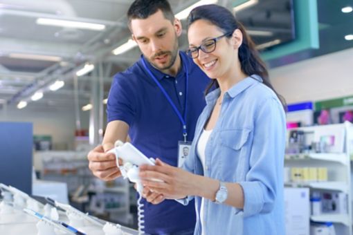 In the Electronics Store Consultant Gives Professional Advice to a Young Woman, She Considers Buying New Tablet Computer and Needs Expert Opinion. Store is Modern, Bright and Has all the New Devices.