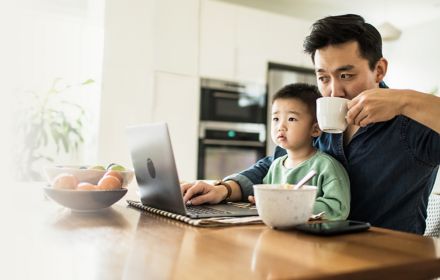 Businessman working from home and drinking coffee with his toddler sitting in lap