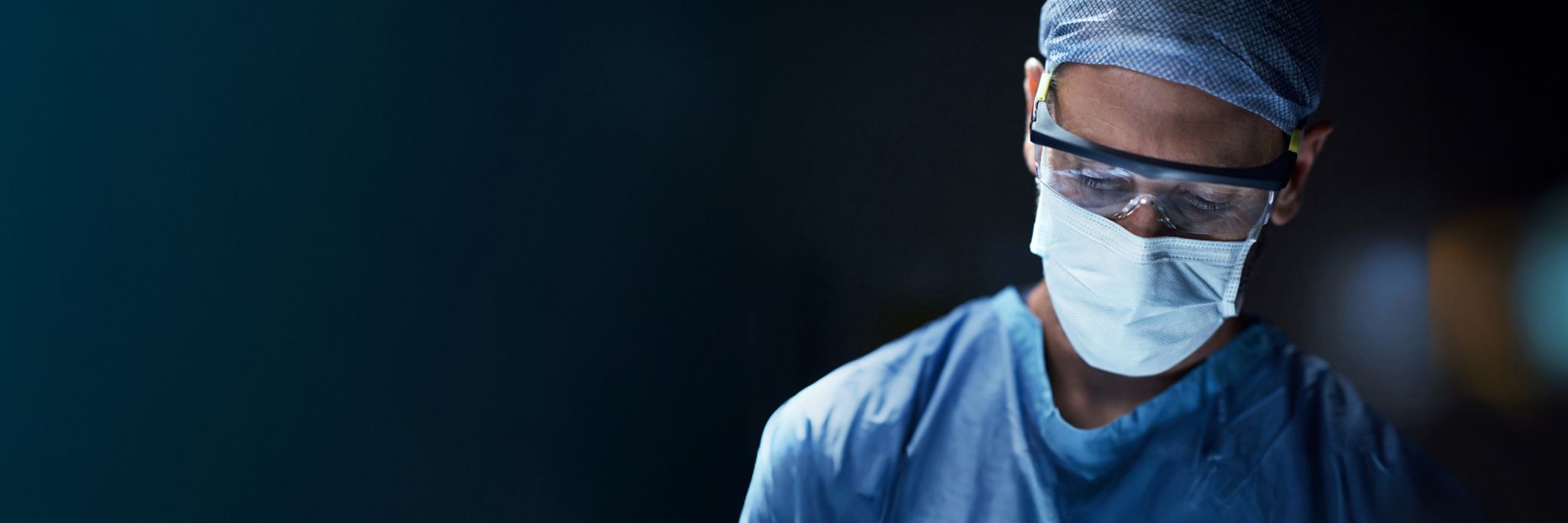 Surgeon in an operating theatre wearing surgical mask, cap and glasses