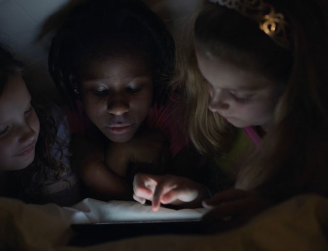 Three kids using a tablet in bed