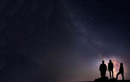 Three people standing under start in night sky