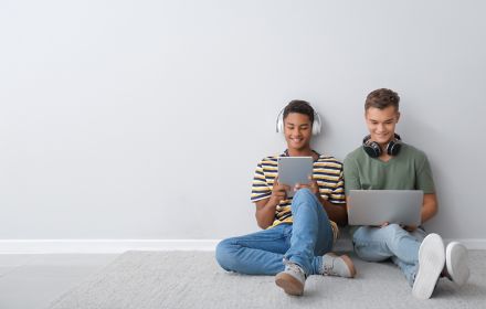 Two boys listening music and looking at laptop and tablet