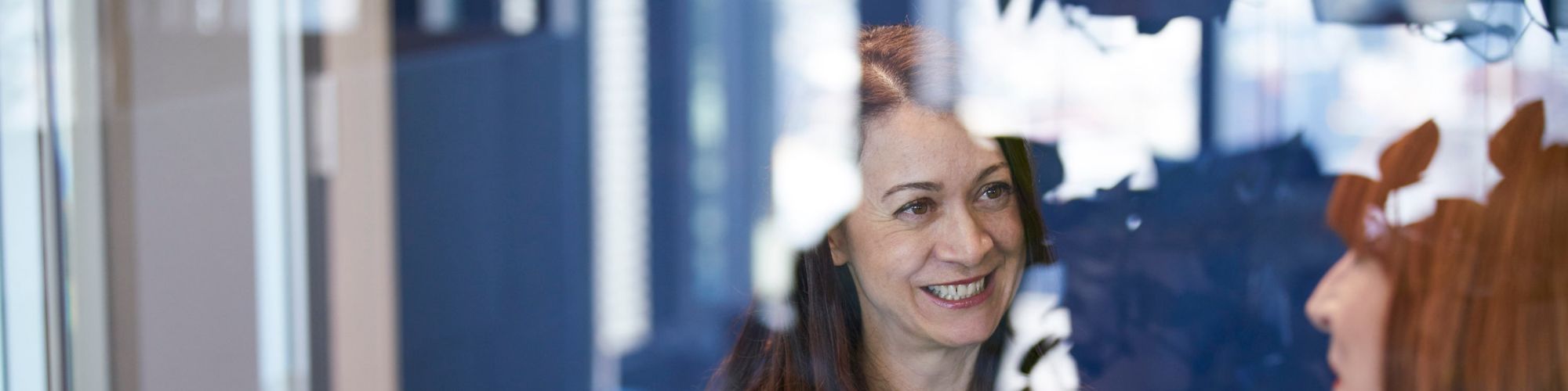 Two woman smiling and discussing behind a big transparent glass window