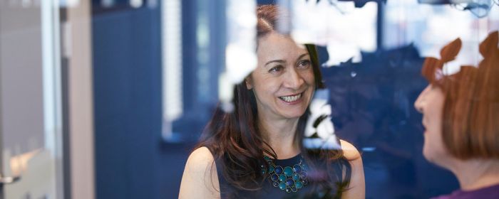 Two woman smiling and discussing behind a big transparent glass window