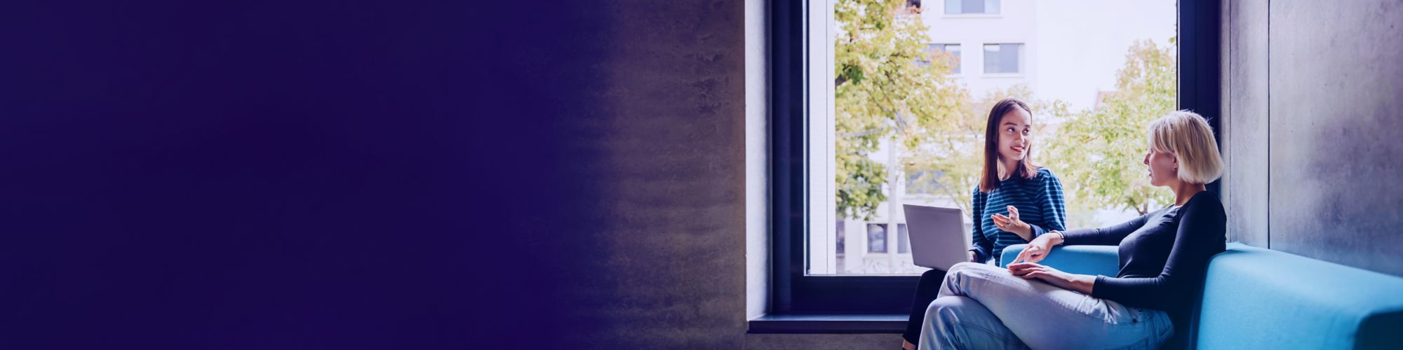 Two women in discussion beside large window