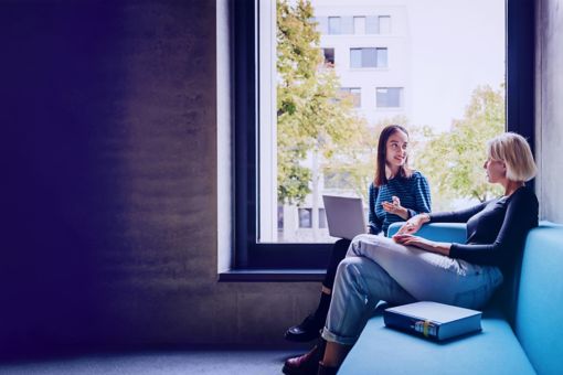 Two women in discussion beside large window