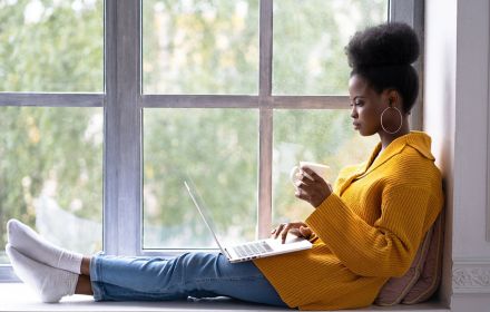 Woman at window with coffee and laptop