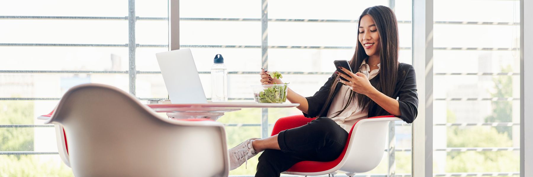Business woman using phone and eating salad