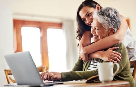Young woman hugging her grandmother before helping her with her finances on a laptop