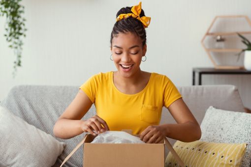 Woman sat on a sofa opening a cardboard box