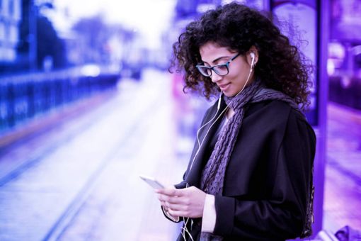 Woman standing looking at her phone next to the train tracks with a purple overlay