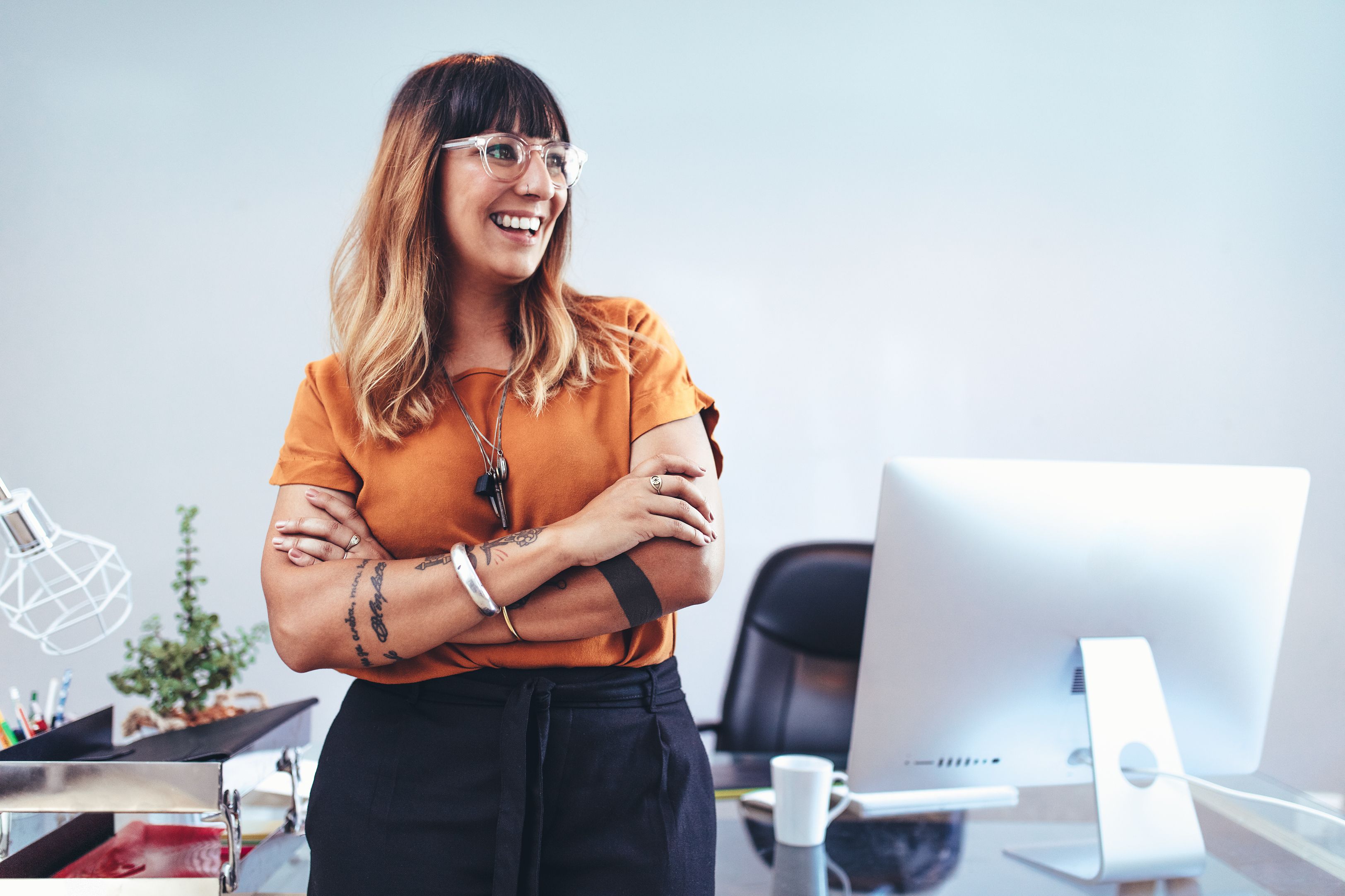 Portrait of a smiling businesswoman standing at her desk in office and looking away. Cheerful woman entrepreneur taking a break from work standing in her cabin at office.