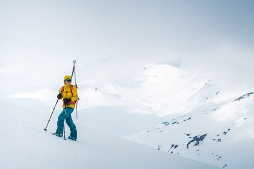 A woman smiles while hiking up a slope with skis on her back