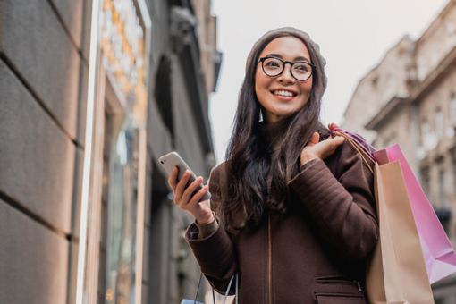 Woman using smartphone and looking away while enjoying a day shopping