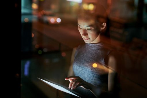 Woman using tablet at night standing near glass window