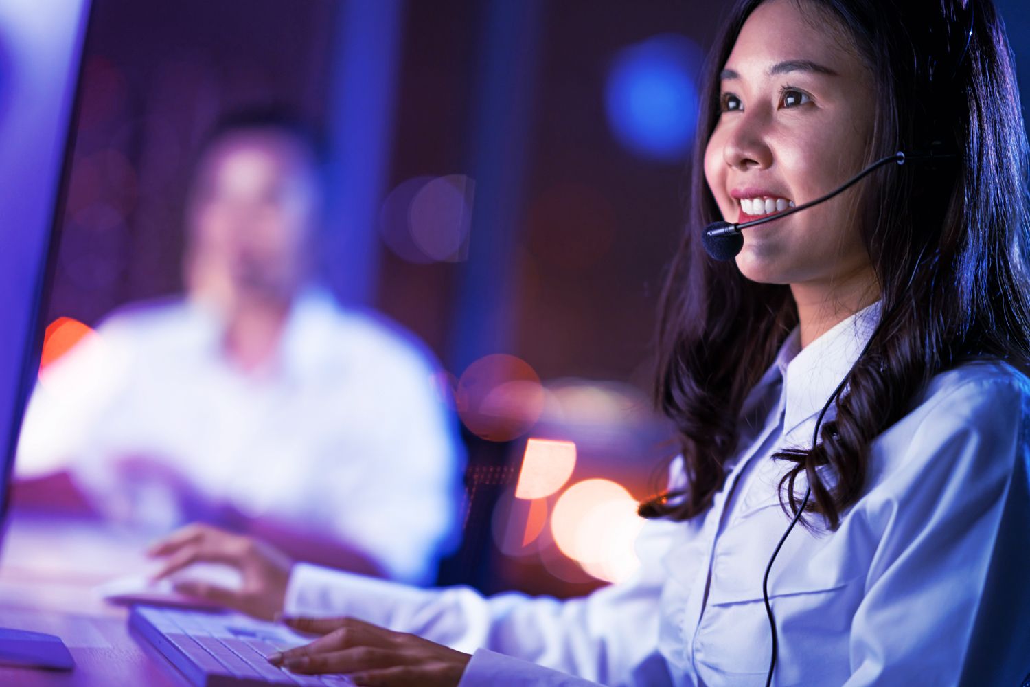 Asian woman work as customer support service or call center phone operator, using desktop computer and microphone headset, late night shift. Overtime office life, telemarketing or sales job concept