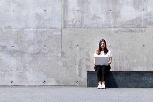 woman with laptop against a concrete wall