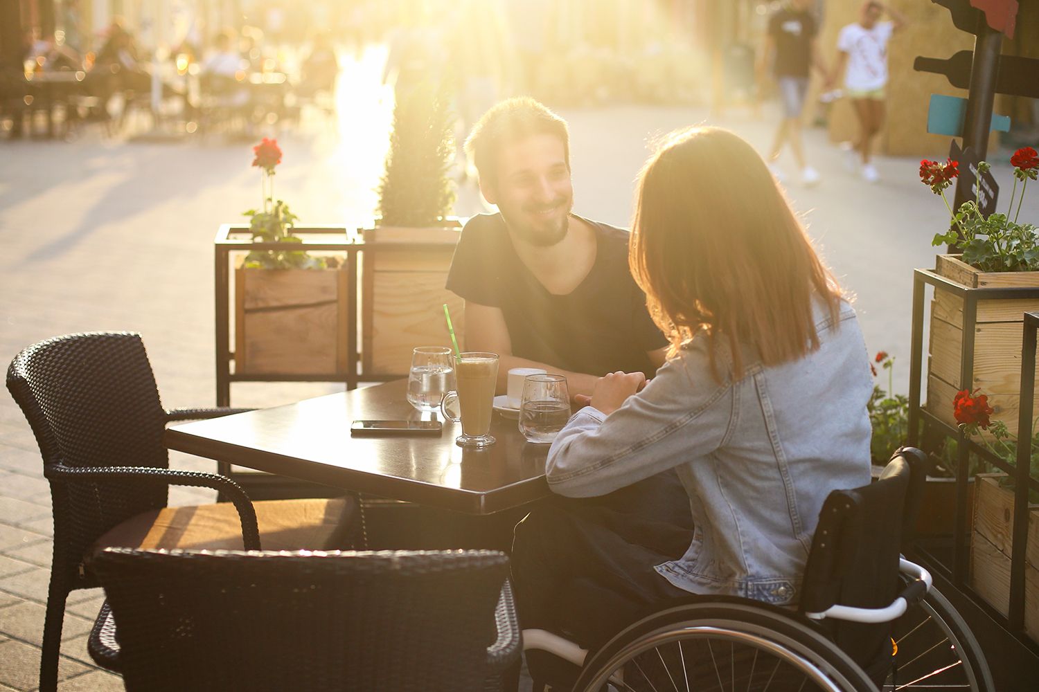 Women with special abilities sitting on a wheel chair while enjoying outside in a café with man and having coffee