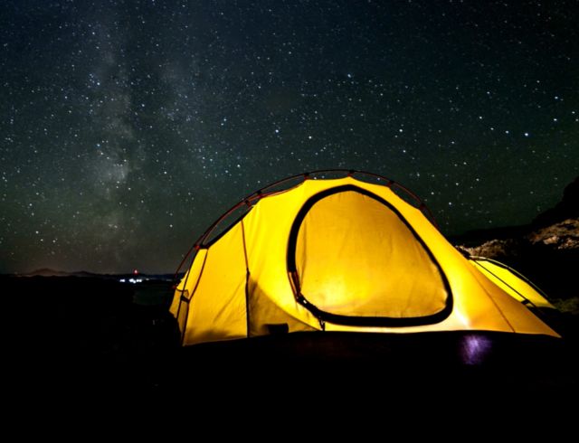Yellow camping and hiking tent at night under shining stars
