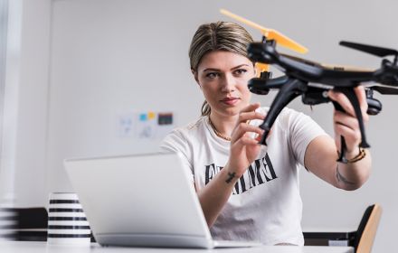 Young woman with laptop at desk holding drone