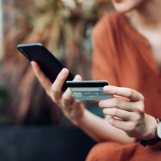 Beautiful smiling young Asian woman relaxing on deck chair in the backyard, surrounded by beautiful houseplants. Shopping online on smartphone and making mobile payment with credit card. Technology makes life so much easier. Lifestyle and technology