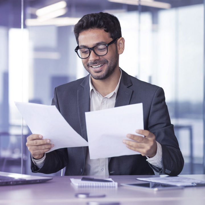 Hombre sentado en oficina leyendo documentos y sonriendo