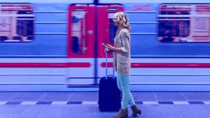 Fotografía de una mujer de pie esperando con su maleta para abordar en la estación de trenes