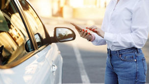 vrouw met telefoon in zijn hand naast een auto