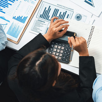 A person is writing on a paper, calculating things on a calculating and looking at graphs on paper.