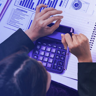 A person is writing on a paper, calculating things on a calculating and looking at graphs on paper.