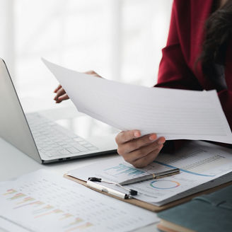 A woman is sitting behind her laptop holding papers