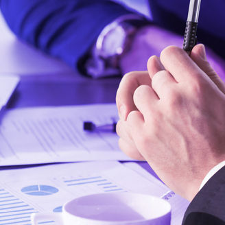 A hand of a man is holding a pen and some papers are visible in the background