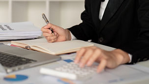 Une personne écrit quelque chose sur un papier et fait des calculs sur une calculatrice