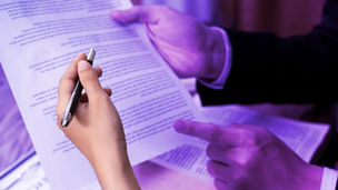 Two people are holding papers and pointing with a pen