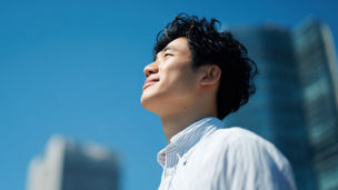 A man is smiling and looking up at the sky. The sky is blue and clear. The man is wearing a white shirt and has short hair
