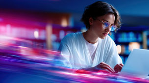 Young woman working on a laptop in a modern office environment with vibrant neon lights and blurred motion effects for technology and innovation themes.