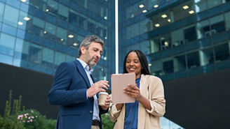 Diverse business people collaborating on a digital tablet in front of a modern office building