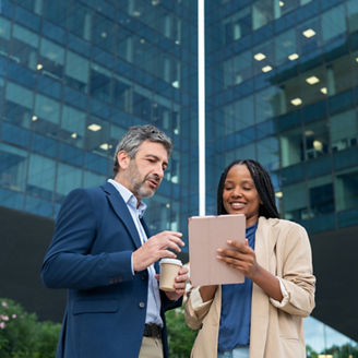 Diverse business people collaborating on a digital tablet in front of a modern office building