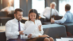 Two elegant partners sitting in airport waiting-room and looking through financial documents before flight
