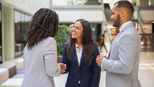 Positive multiethnic business partners greeting each other. Business man and women standing in office hall, shaking hands, talking, smiling. Collaboration concept